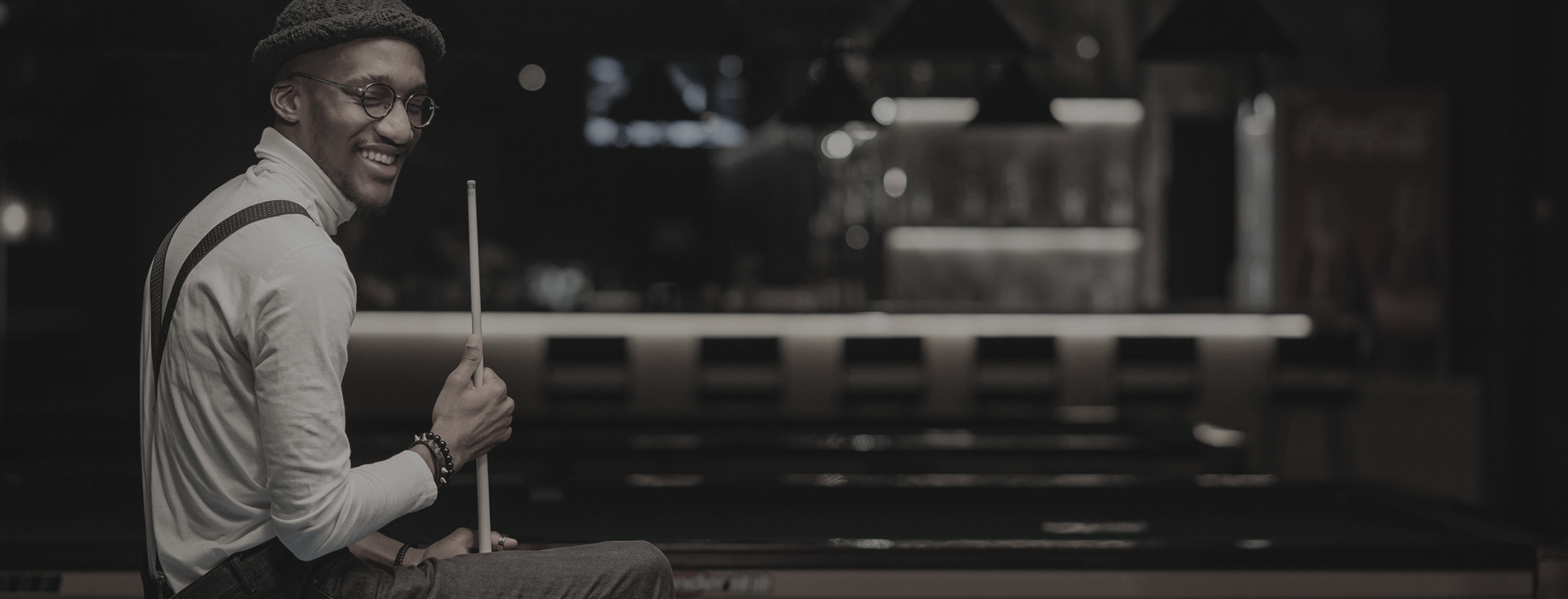 Man smiling while holding a pool cue in a dimly lit bar.