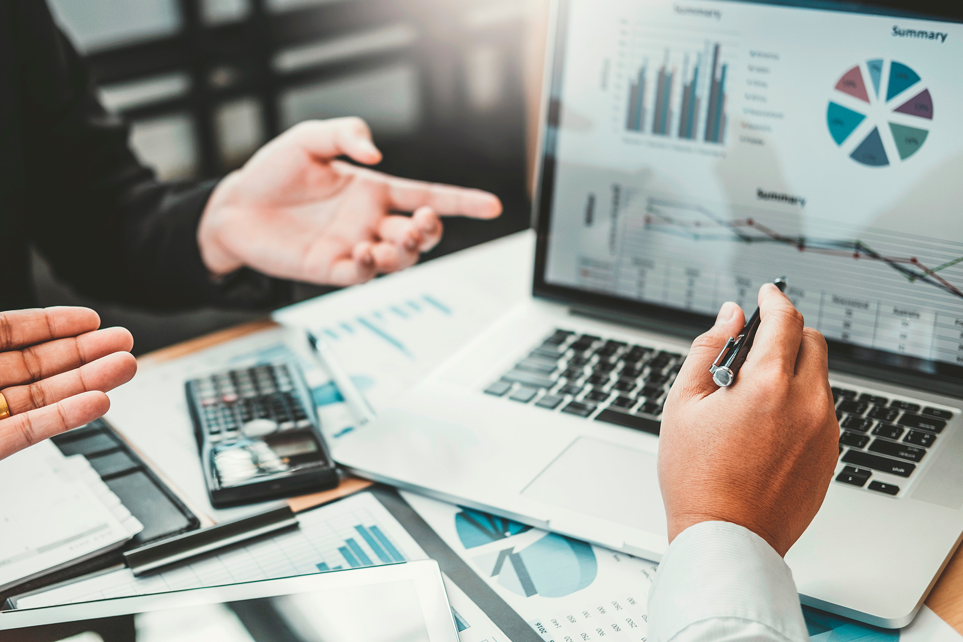 Two people analyzing graphs and charts on a laptop and printed documents.