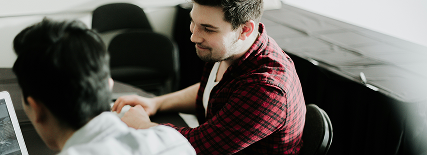 Two men talking at a table, one using a laptop.